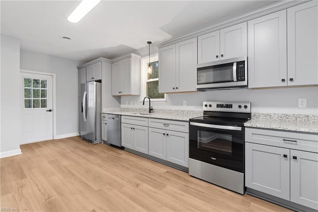 kitchen with light stone counters, appliances with stainless steel finishes, sink, and light hardwood / wood-style flooring