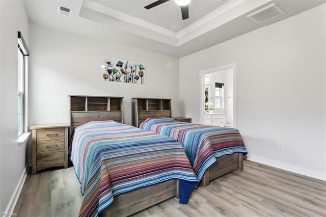 bedroom featuring wood finished floors, a raised ceiling, visible vents, and baseboards