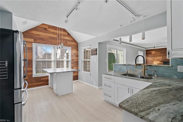 kitchen featuring sink, stainless steel refrigerator, white cabinetry, a center island, and decorative light fixtures