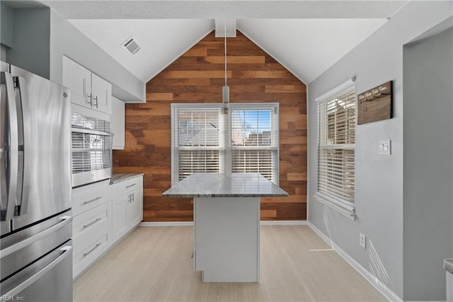 kitchen featuring light stone countertops, a kitchen island, white cabinets, and stainless steel refrigerator