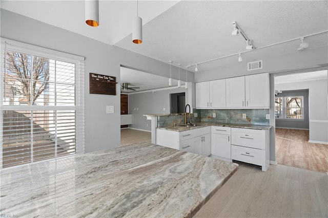 kitchen featuring light stone counters, decorative light fixtures, light hardwood / wood-style flooring, kitchen peninsula, and white cabinets