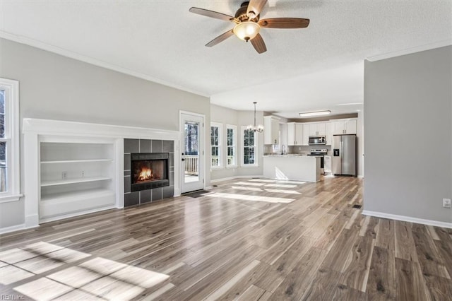 unfurnished living room featuring a tile fireplace, ornamental molding, light hardwood / wood-style floors, a textured ceiling, and ceiling fan with notable chandelier