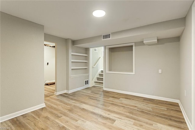 basement with built in shelves and light hardwood / wood-style flooring