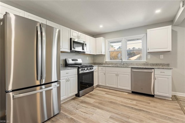 kitchen featuring appliances with stainless steel finishes, white cabinetry, sink, light stone counters, and light hardwood / wood-style flooring