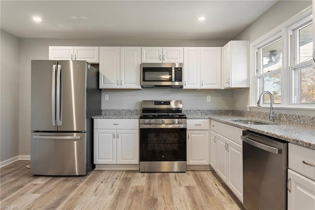 kitchen featuring sink, light stone counters, stainless steel appliances, light hardwood / wood-style floors, and white cabinets