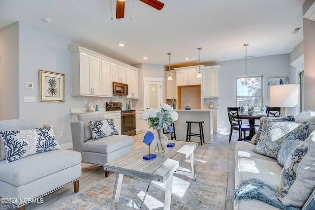 living room featuring ceiling fan with notable chandelier and light hardwood / wood-style floors