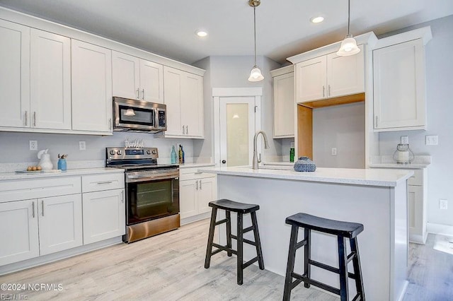 kitchen with pendant lighting, light hardwood / wood-style flooring, white cabinetry, a kitchen island with sink, and stainless steel appliances