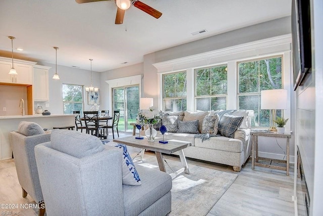 living room with ceiling fan with notable chandelier, sink, and light hardwood / wood-style flooring