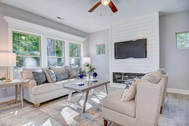 living room with light hardwood / wood-style flooring, a large fireplace, and ceiling fan