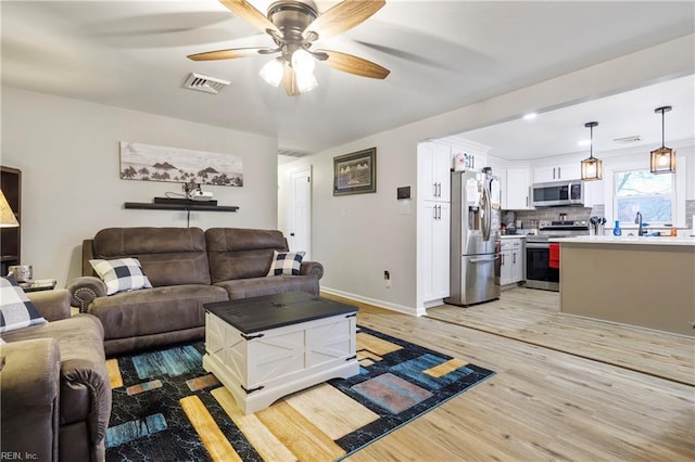 living room with ceiling fan, sink, and light wood-type flooring