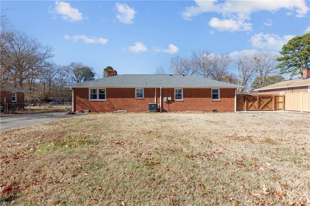 rear view of house with central AC unit and a lawn