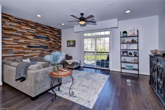 living room with dark wood-type flooring, ceiling fan, and wood walls