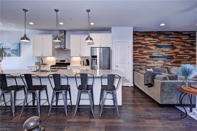 kitchen featuring sink, pendant lighting, stainless steel appliances, a kitchen island with sink, and wall chimney range hood