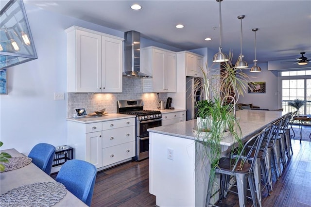 kitchen with white cabinets, hanging light fixtures, stainless steel appliances, a center island with sink, and wall chimney exhaust hood