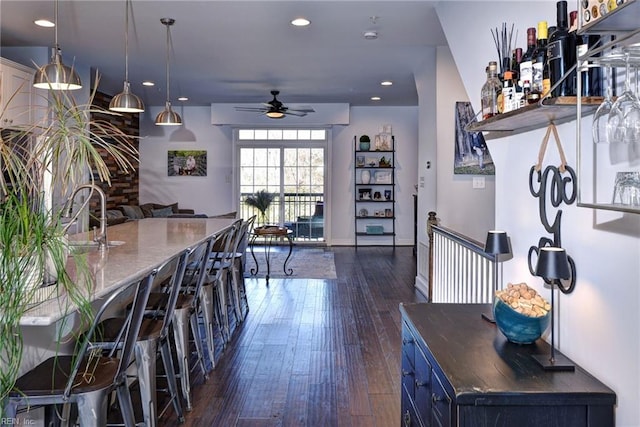 kitchen featuring blue cabinets, a breakfast bar area, hanging light fixtures, ceiling fan, and dark wood-type flooring