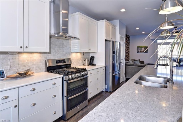 kitchen featuring sink, appliances with stainless steel finishes, wall chimney range hood, decorative backsplash, and white cabinets