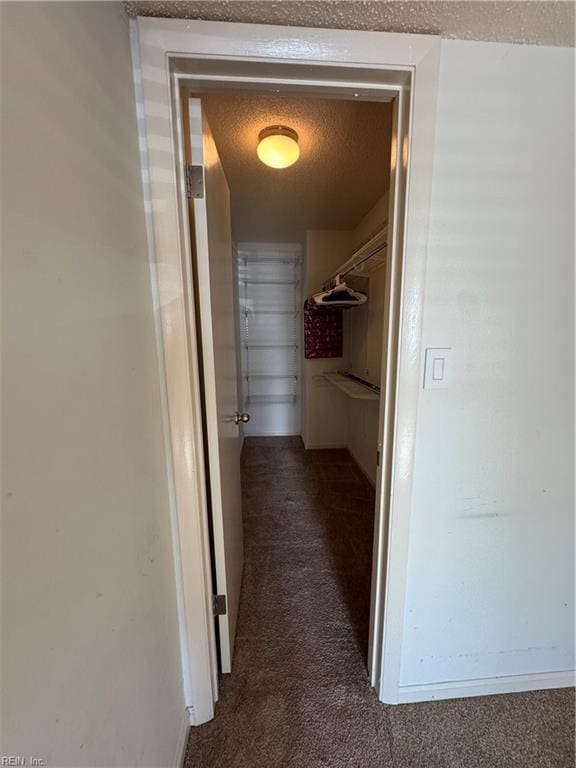 corridor with dark colored carpet and a textured ceiling