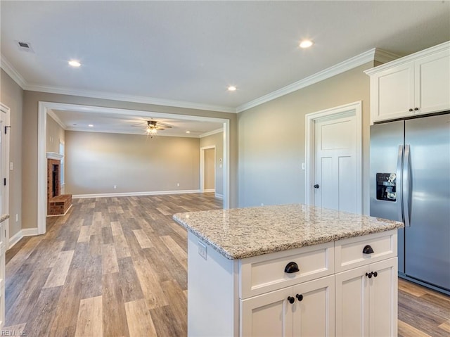 kitchen with stainless steel refrigerator with ice dispenser, light stone counters, light hardwood / wood-style floors, white cabinets, and a brick fireplace