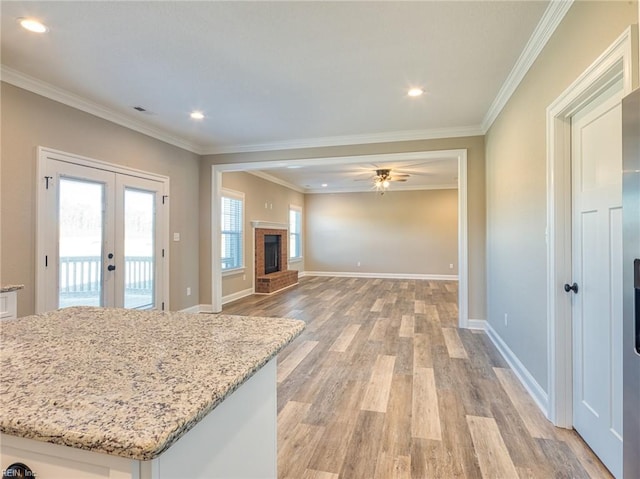 kitchen with french doors, light stone counters, white cabinetry, light wood-type flooring, and a fireplace