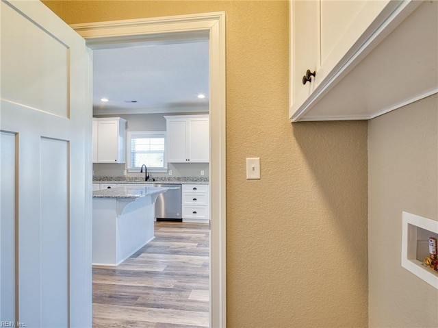 kitchen with white cabinetry, a kitchen breakfast bar, stainless steel dishwasher, light stone counters, and light hardwood / wood-style flooring