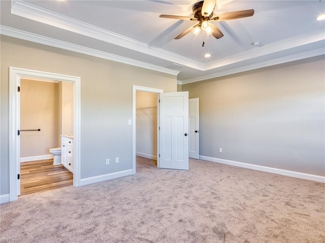 unfurnished bedroom featuring a walk in closet, a raised ceiling, crown molding, light carpet, and ensuite bath