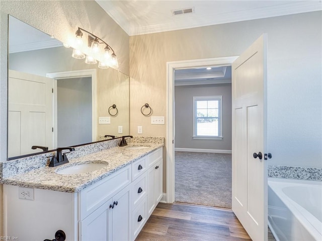 bathroom featuring ornamental molding, wood-type flooring, vanity, and a tub