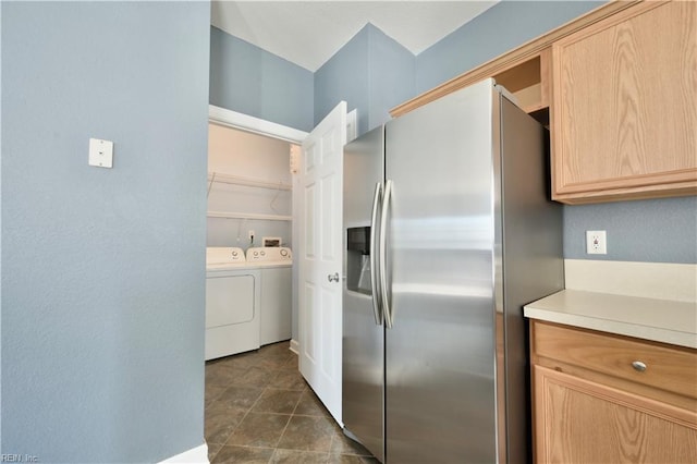 kitchen with light brown cabinets, washer and dryer, dark tile patterned floors, and stainless steel refrigerator with ice dispenser