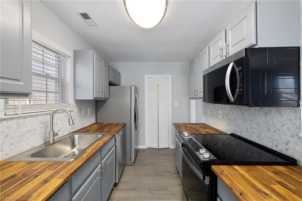 kitchen featuring sink, wooden counters, light hardwood / wood-style flooring, appliances with stainless steel finishes, and backsplash