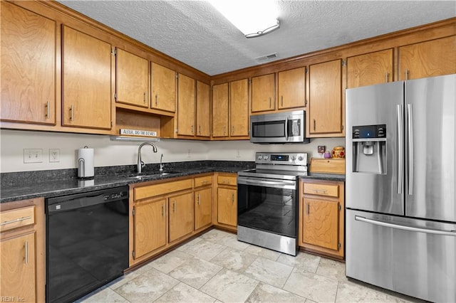 kitchen featuring sink, dark stone counters, a textured ceiling, and appliances with stainless steel finishes