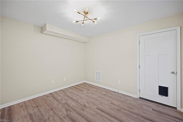 empty room with a notable chandelier, wood finished floors, visible vents, and baseboards