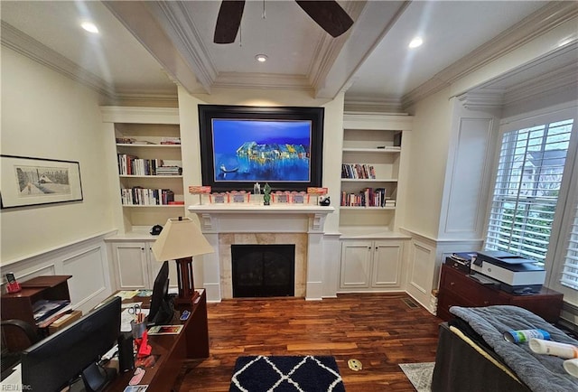 living room with built in shelves, ornamental molding, dark hardwood / wood-style flooring, a tile fireplace, and ceiling fan