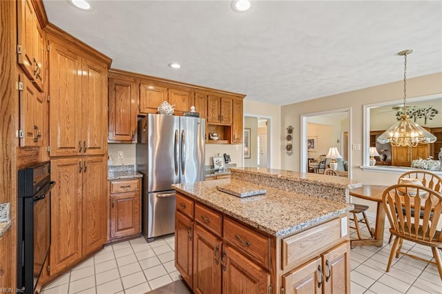 kitchen with black oven, stainless steel refrigerator, decorative light fixtures, a center island, and light stone counters