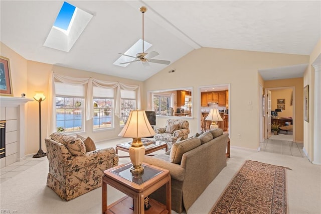 living room featuring ceiling fan, light colored carpet, vaulted ceiling with skylight, and a tiled fireplace