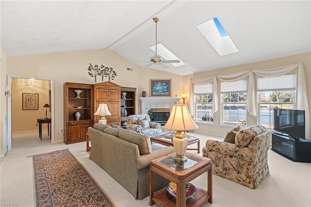 living room featuring ceiling fan, light colored carpet, lofted ceiling with skylight, and a tile fireplace