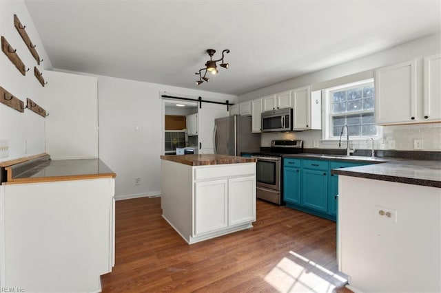 kitchen featuring appliances with stainless steel finishes, white cabinetry, blue cabinets, dark hardwood / wood-style flooring, and a barn door