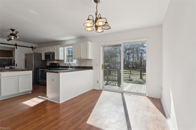 kitchen featuring dark hardwood / wood-style flooring, pendant lighting, stainless steel appliances, a barn door, and white cabinets