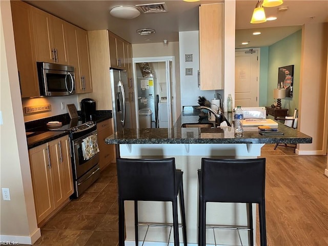 kitchen featuring a kitchen bar, sink, stainless steel appliances, kitchen peninsula, and hanging light fixtures