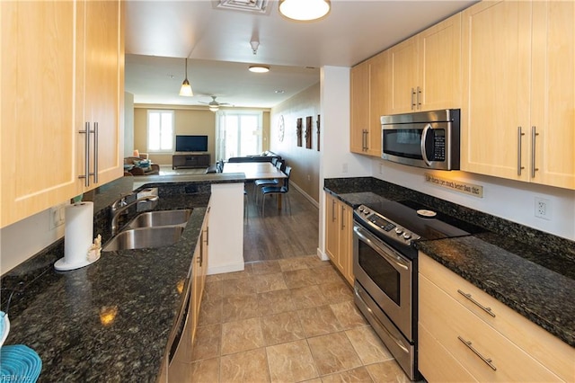 kitchen with decorative light fixtures, sink, stainless steel appliances, and dark stone counters