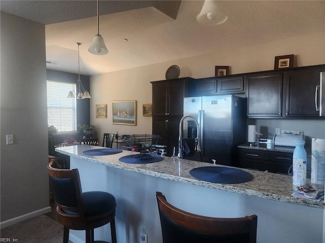 kitchen featuring pendant lighting, a breakfast bar area, dark brown cabinetry, and stainless steel refrigerator with ice dispenser