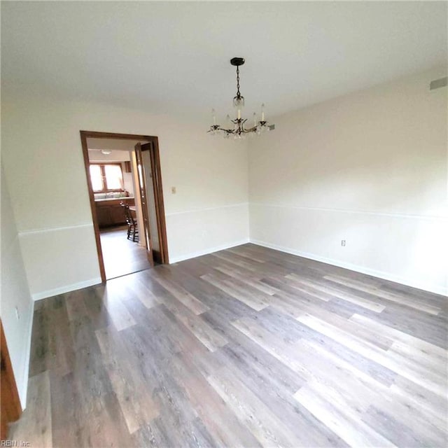 unfurnished dining area with a notable chandelier, baseboards, and wood finished floors