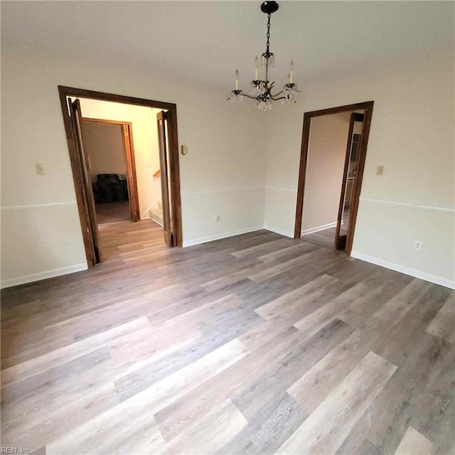 unfurnished dining area with baseboards, an inviting chandelier, and wood finished floors