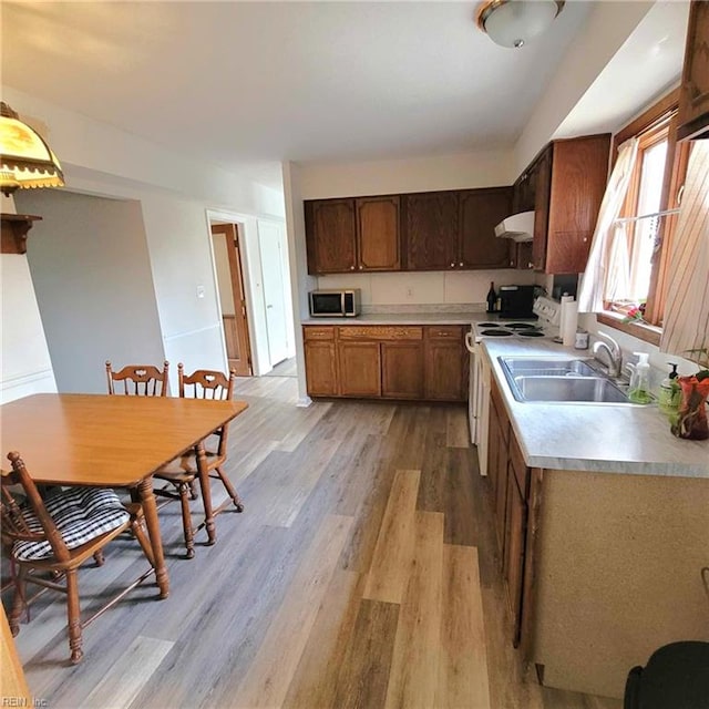 kitchen with white electric stove, a sink, light countertops, light wood-type flooring, and stainless steel microwave