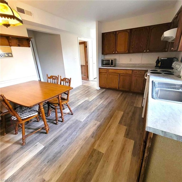 kitchen with light countertops, visible vents, stainless steel microwave, wood finished floors, and under cabinet range hood