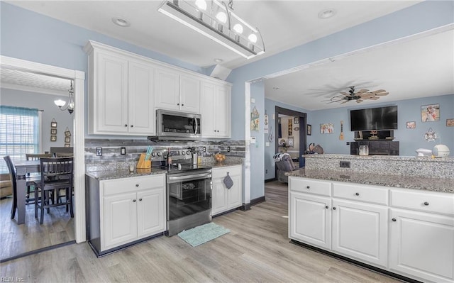 kitchen with appliances with stainless steel finishes, white cabinetry, stone countertops, decorative backsplash, and light wood-type flooring