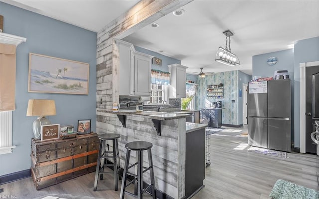 kitchen featuring pendant lighting, stainless steel refrigerator, white cabinetry, a kitchen bar, and kitchen peninsula