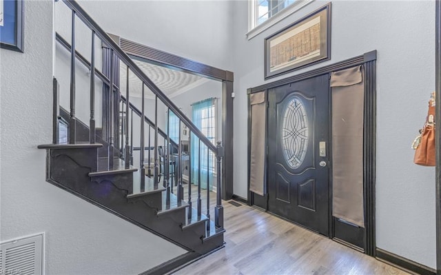 entrance foyer with hardwood / wood-style floors, crown molding, and a towering ceiling