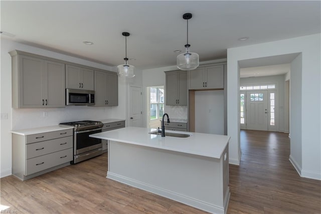 kitchen featuring sink, gray cabinetry, a center island with sink, pendant lighting, and stainless steel appliances