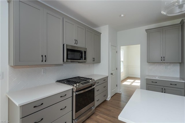kitchen with gray cabinets, appliances with stainless steel finishes, backsplash, and light wood-type flooring