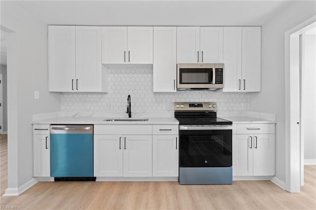 kitchen with appliances with stainless steel finishes, white cabinetry, sink, decorative backsplash, and light wood-type flooring