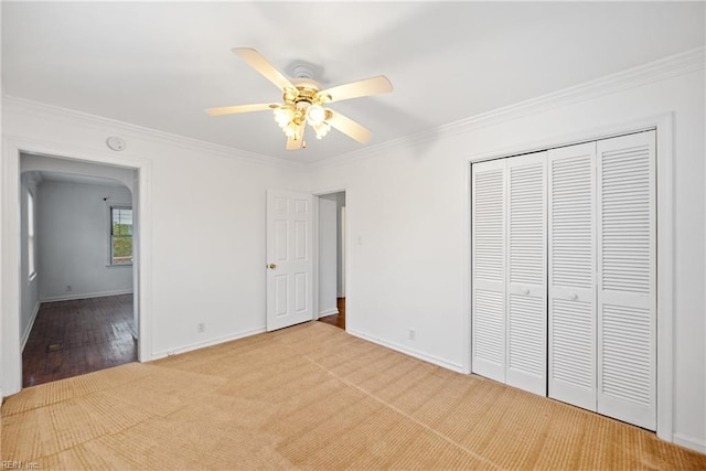 unfurnished bedroom featuring ornamental molding, light carpet, ceiling fan, and a closet